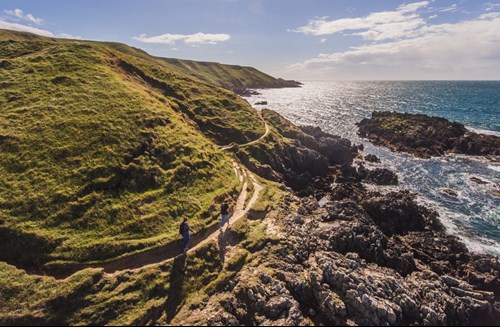 A Pair Of Walkers On The Wales Coastal Path At Porthor, Llŷn Peninsula Where Rugged Green Hills Meet The Sea